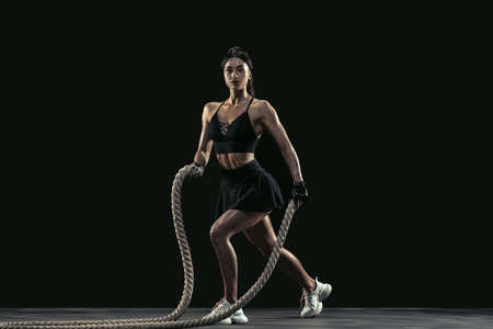 Beautiful young female athlete practicing on black studio background, full length portrait. Sportive...