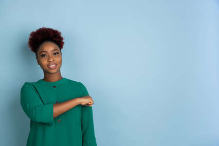 Fist bump at side, smiling. African-american young womans portrait isolated on blue studio background. Beautiful female model. Concept of human emotions, facial expression, sales, ad. Copyspace.の写真素材