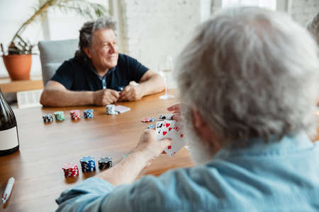 Young at heart. Two happy mature friends playing cards and drinking wine. Look delighted, excited. Caucasian men gambling at home. Sincere emotions, wellbeing, facial expression concept. Good old age.の写真素材