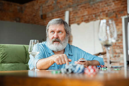Exciting. Happy mature man playing cards and drinking wine with friends. Looks delighted, excited....
