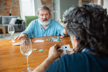 Young at heart. Two happy mature friends playing cards and drinking wine. Look delighted, excited. Caucasian men gambling at home. Sincere emotions, wellbeing, facial expression concept. Good old age.の写真素材