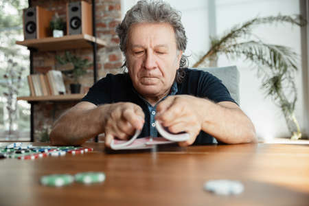 Exciting. Happy mature man playing cards and drinking wine with friends. Looks delighted, excited. Caucasian man gambling at home. Sincere emotions, wellbeing, facial expression concept. Good old age.の写真素材