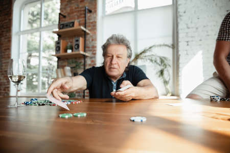 Exciting. Happy mature man playing cards and drinking wine with friends. Looks delighted, excited. Caucasian man gambling at home. Sincere emotions, wellbeing, facial expression concept. Good old age.の写真素材