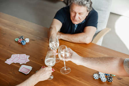 Top view group of happy mature friends playing cards and drinking wine, clinking glasses. Look delighted, excited. Caucasian men gambling at home. Sincere emotions, wellbeing, facial expression concept.の写真素材