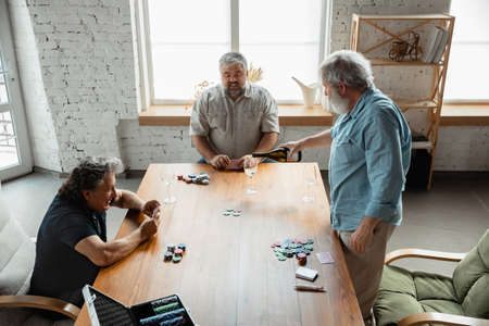 Always young. Group of happy mature friends playing cards and drinking wine. Look delighted, excited. Caucasian men gambling at home. Sincere emotions, wellbeing, facial expression concept.の写真素材