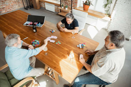 Always young. Group of happy mature friends playing cards and drinking wine. Look delighted,...