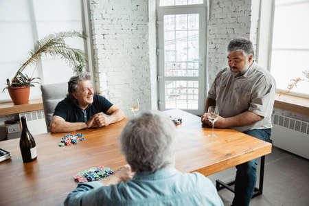 Always young. Group of happy mature friends playing cards and drinking wine. Look delighted, excited. Caucasian men gambling at home. Sincere emotions, wellbeing, facial expression concept.の写真素材