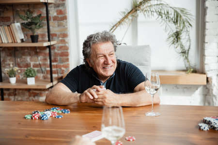 Exciting. Happy mature man playing cards and drinking wine with friends. Looks delighted, excited. Caucasian man gambling at home. Sincere emotions, wellbeing, facial expression concept. Good old age.の写真素材