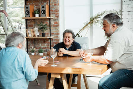 Always young. Group of happy mature friends playing cards and drinking wine. Look delighted, excited. Caucasian men gambling at home. Sincere emotions, wellbeing, facial expression concept.の写真素材