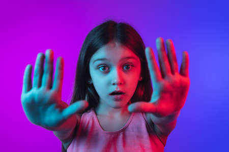 Giving palms, hopeful. Little girls portrait on gradient pink-blue studio background in neon. Concept of human emotions, facial expression, modern gadgets and tech, sales, ad. Copyspace.の写真素材
