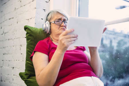 Mature woman spending time being quarantined - caucasians woman using modern gadgets, drinking tea. Eyes tired of gadgets using. Interested and having fun. Copyspace on blank screen. Lifestyle.の写真素材