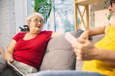 Wondered. Couple of seniors spending time together being quarantined - caucasians mature and retired man and woman using modern gadgets, talking, drinking tea. Eyes tired of gadgets life. Lifestyle.の写真素材