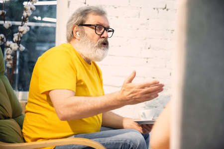 Cozy talking. Couple of seniors spending time together being quarantined - mature and retired man and woman discussing, talking, drinking tea. Eyes tired of gadgets. Cozy domestic evening. Lifestyle.の写真素材