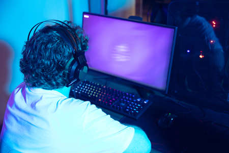 Cyber sport. Copyspace on monitor, screen. Fully concentrated professional gamer playing important match. Caucasian man practicing before tournament alone in neon light. E-sport, gamer, streamer.の写真素材