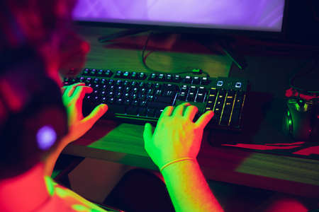 Cyber sport. Fully concentrated professional cybersport gamer playing important match. Caucasian male model practicing before tournament alone in neon light. E-sport, gamer, streamer. Close up.の写真素材