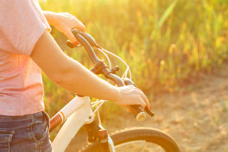 Close up joyful young woman riding a bicycle at the riverside and meadow promenade. Inspired by surrounded nature, summertime mood. Warm sunshine colors. Sport, activity, wellness, enjoyment concept.の写真素材