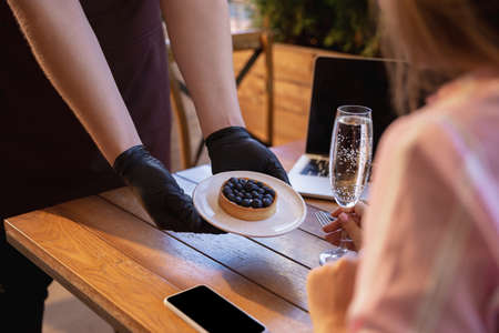 The waiter works in a restaurant in a medical mask, gloves during coronavirus pandemic. Representing...