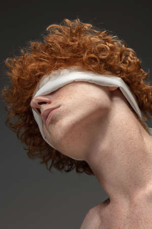 Going blind. Fashion portrait of beautiful redhead man isolated on grey studio background. Concept of beauty, skin care, fashion and style. Artwork, modern and trendy portrait. Attractive model.の写真素材