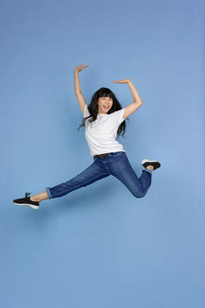 Jumping high, looks emotional, happy, cheerful. Portrait of young asian woman isolated on blue background. Beautiful cute girl. Human emotions, facial expression, sales, ad, online shopping concept.の写真素材