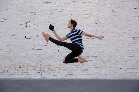 Jumping young buinessman in front of city building wall, on the run in jump high. Reading news,...
