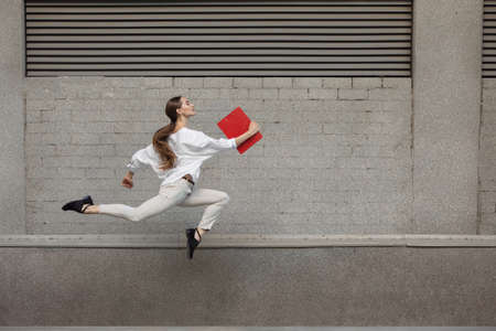Paperwork. Jumping young woman in front of city building wall, on the run in jump high. Hurrying up...