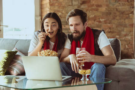 Excited football fans watching sport match at home, remote support of favourite team during...