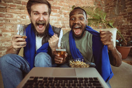Excited football fans watching sport match at home, remote support of favourite team during...