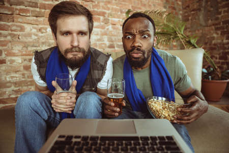 Excited football fans watching sport match at home, remote support of favourite team during...