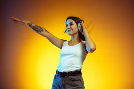 Pointing. Portrait of young caucasian woman isolated on gradient yellow studio background. Stylish,...