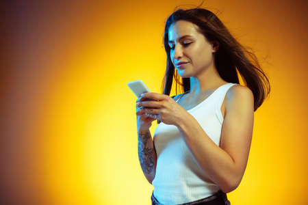 Typing. Portrait of young caucasian woman isolated on gradient yellow studio background. Stylish,...