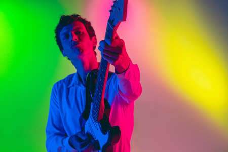 Close up. Young caucasian inspired and expressive musician, guitarist performing on multicolored...