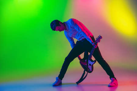 Talented. Young caucasian inspired and expressive musician, guitarist performing on multicolored...