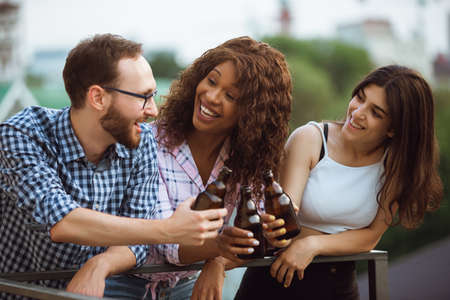 Group of happy friends having beer party in summer day. Resting together outdoor, celebrating and relaxing, laughting. Summer lifestyle, friendship concept. Clinking beers bottles, cheerful, happy.の写真素材