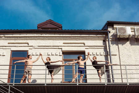 The group of modern ballet dancers performing on the stairs at the city. Fast moving of citylife, grace in daily things around. Graceful and flexible models in sunshine with buildings on background.の写真素材