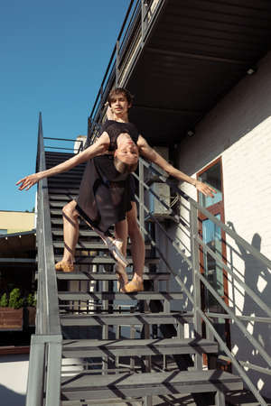 Couple of modern ballet dancers performing on the stairs at the city. Fast moving of citylife, grace in daily things around. Graceful and flexible models in sunshine with buildings on background.の写真素材