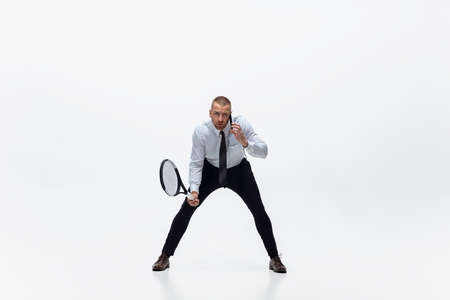 Time for movement. Man in office clothes plays tennis isolated on white studio background. Businessman training in motion, action. Unusual look for sportsman, new activity. Sport, healthy lifestyle.の写真素材