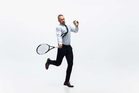 Time for movement. Man in office clothes plays tennis isolated on white studio background. Businessman training in motion, action. Unusual look for sportsman, new activity. Sport, healthy lifestyle.の写真素材