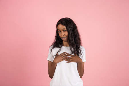 Shy. Cheerful african-american young woman isolated on pink background, emotional and expressive. Concept of human emotions, facial expression, sales, ad. Beautiful model with long curly hair.の写真素材