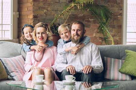 Memory. Happy family traditional portrait, old-fashioned. Cheerful parents and kids in official styled attire on dark vintage background. Concept of human emotions, memories, togetherness, fun.の写真素材