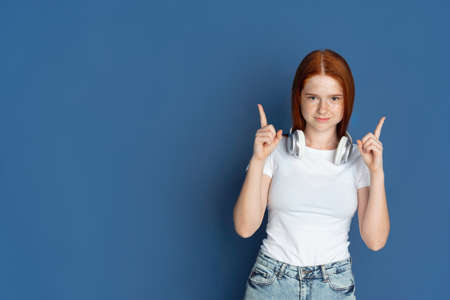 Pointing, choosing. Caucasian young girls portrait on blue background. Beautiful female redhair...