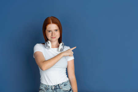 Pointing, choosing. Caucasian young girls portrait on blue background. Beautiful female redhair model with cute freckles. Concept of human emotions, facial expression, sales, ad, youth culture.の写真素材