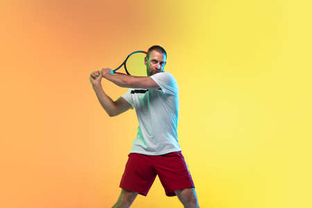One caucasian man playing tennis isolated on studio background in neon light. Fit young professional...