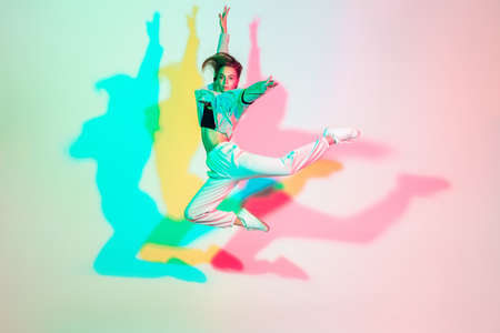 Young beautiful woman dancing hip-hop, street style isolated on studio background in colorful neon light. Fashion and motion, youth, music, action concept. Trendy clothes. Copyspace for ad.の写真素材