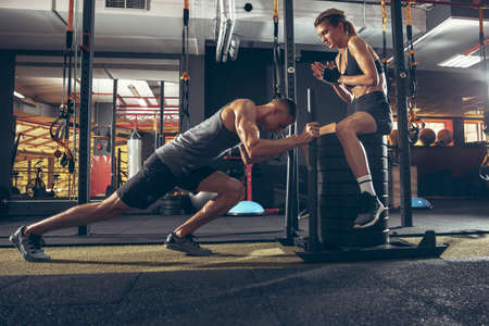 Beautiful young sporty couple workout in gym together. Caucasian man training with female trainer. Concept of sport, activity, healthy lifestyle, strength and power. Working out with weights.の写真素材