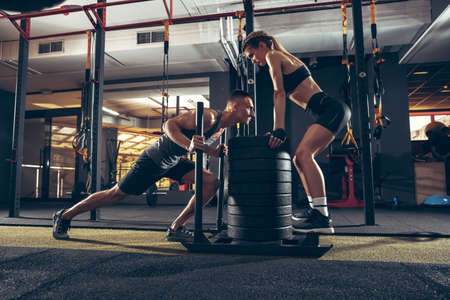 Beautiful young sporty couple workout in gym together. Caucasian man training with female trainer. Concept of sport, activity, healthy lifestyle, strength and power. Working out with weights.の写真素材