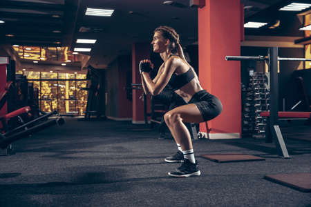Beautiful young sporty woman workout in gym. Caucasian female trainer. Concept of sport, activity, healthy lifestyle, strength and power. Working out sit ups with weights, shows how to do it right.の写真素材