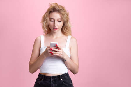 Scrolling phone. Caucasian young womans portrait isolated on pink studio background. Beautiful...