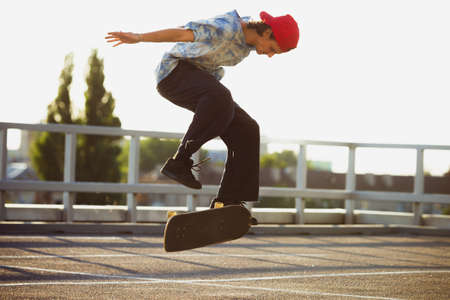 Skateboarder doing a trick at the city's street in summer's sunshine. Young man in sneakers and cap riding and skateboarding on the asphalt. Concept of leisure activity, sport, extreme, hobby and motion.の写真素材