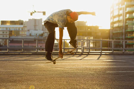 Skateboarder doing a trick at the city's street in summer's sunshine. Young man in sneakers and cap riding and skateboarding on the asphalt. Concept of leisure activity, sport, extreme, hobby and motion.の写真素材