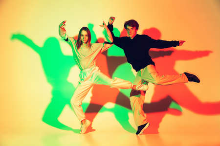 Young man and woman, couple dancing hip-hop, street style isolated on studio background in colorful neon light. Fashion and motion, youth, music, action concept. Trendy clothes. Copyspace for ad.の写真素材